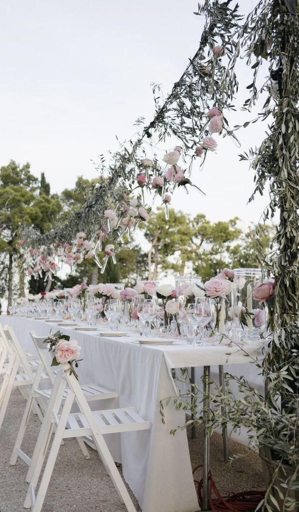 Lange bruiloftstafel onder olijftakken met roze rozen